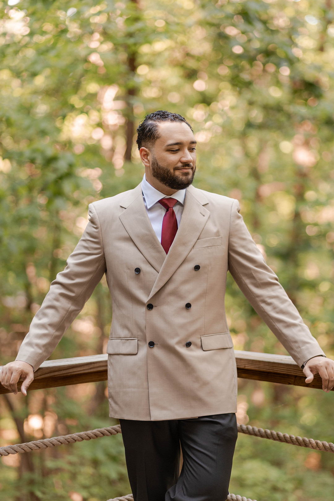 Groom in a double-breasted tan suit and burgundy tie on the deck
