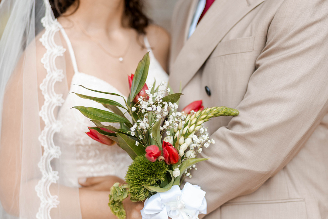 Close-up of the bride's red rose bouquet against the groom's tan suit