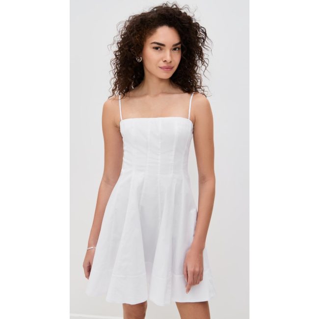 Model in the white STAUD Wylie mini dress with thin straps, a fitted bodice and a flared skirt