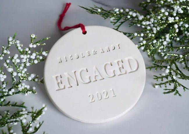 Ivory earthenware ornament stamped with ENGAGED and a year in raised letters, beside white baby's breath