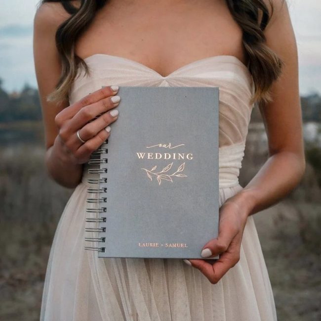 Woman holding a ThePaperMemory gray spiral wedding planner with Wedding in gold foil