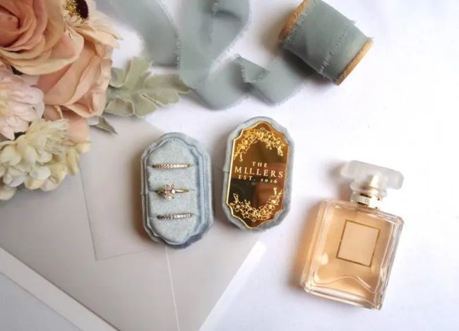 TheQuinnandCompany velvet ring boxes with mirrored monogram lids in blue and gold, beside a perfume bottle