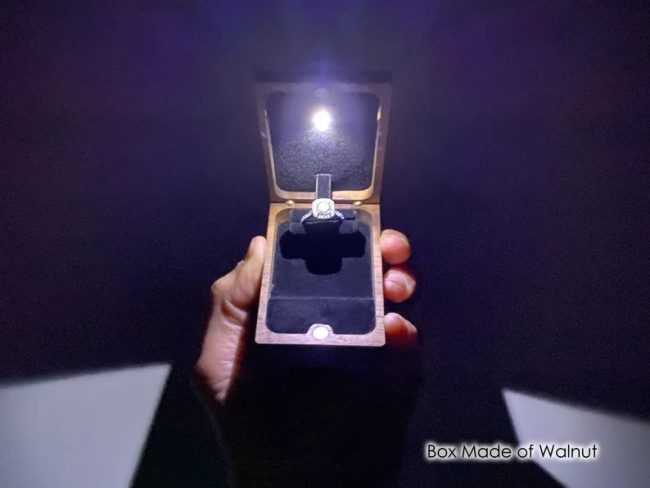 Hand holding a Wanderweg walnut flip-up ring box with its LED light on in a dark room